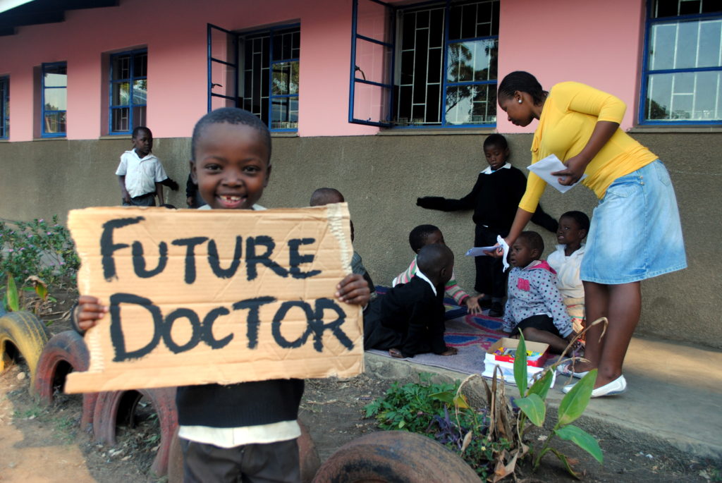 Young boy holding board to communicate he wants to be a doctor in his future